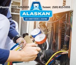 hand holding gauges attached to AC unit with Alaskan Air Conditioning and Heating logo and contact phone numbers across top