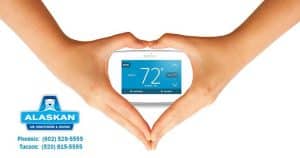 hands coming down over thermostat to make hands into heart around thermostat, Alaskan Air Conditioning and Heating logo and contact phone numbers in bottom left corner