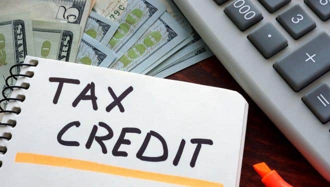 Tax Credit written on spiral paper, cash and calculator in background