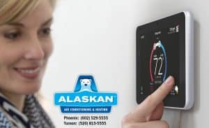 Woman smiling while adjusting digital thermostat, Alaskan Air Conditioning and Heating logo and contact phone numbers in bottom middle section of image